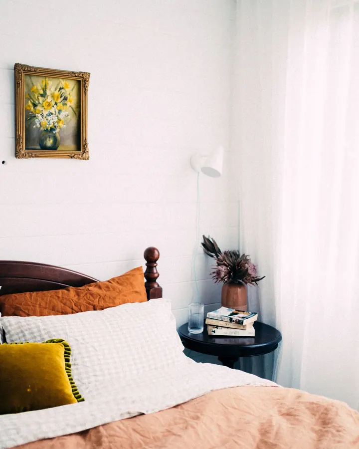 Bed with a wooden frame, linen and a small round bedside table