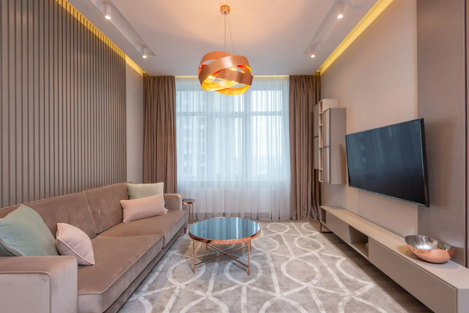Living room with a long beige sofa, wood slat panelling and a copper pendant light